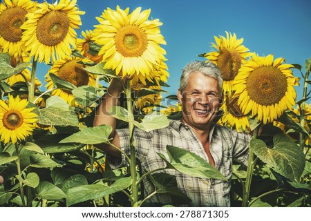 Farmer in a sunflower field. Senior farmer man is standing and smiling in a sunflower field with a blue sky background. Agriculture and nature concept.