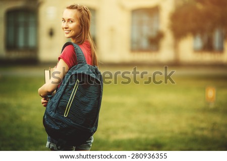 Student girl outside in summer park smiling happy. Caucasian college or university student. Young woman model wearing school bag outdoors in campus.