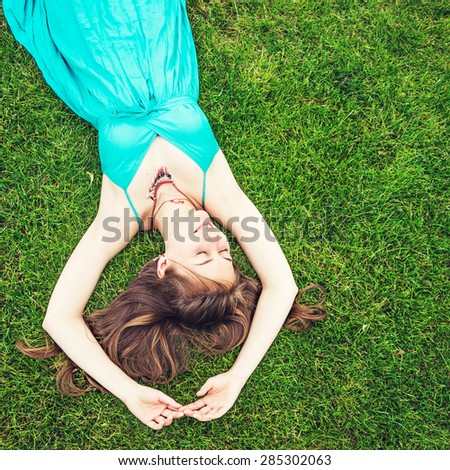 Relaxing young woman on a green grass outdoors. Concept of a relaxation in the spring or summer park.