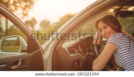 Traveler woman resting on a car wheel during a stop on road trip vacation travel. Young woman relaxing in the car with sunlit backlit road in background.