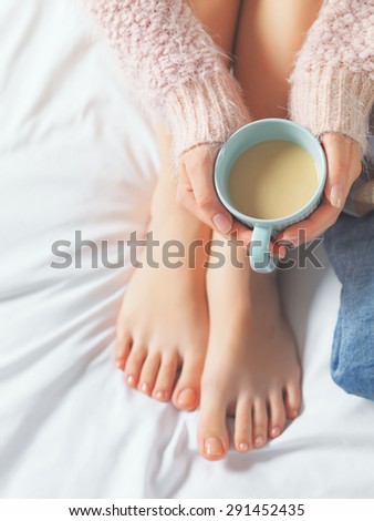 Woman relaxing at cozy home atmosphere on the bed. Young woman with beautiful skin and nails with cup of cocoa or coffee in her hands enjoying comfort. Soft light and comfy beauty natural lifestyle.