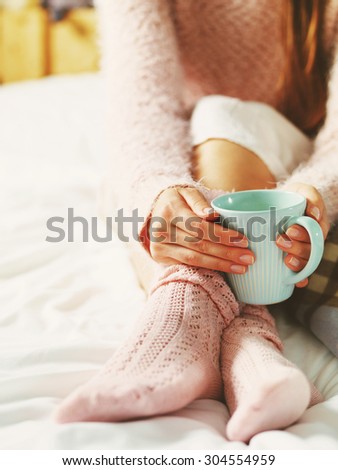 Woman relaxing at cozy home atmosphere on the bed. Young woman with cup of milk in hands enjoying comfort. Soft light and comfy lifestyle concept.