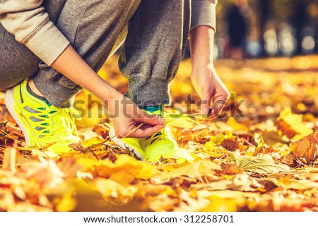 Running shoes. Barefoot running shoes closeup. Female athlete tying laces for jogging on autumn road in minimalistic barefoot running shoes. Runner getting ready for training in fall. Sport lifestyle.