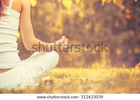Yoga outdoors in warm autumn park. Woman sits in lotus position zen gesturing. Concept of healthy lifestyle and relaxation