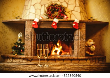 Two glasses of sparkling champagne in front of warm fireplace. Cozy relaxed magical atmosphere in a chalet house by the fireside. Snug holiday concept. Beautiful background with shimmering wine.