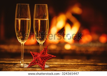 Two glasses of sparkling champagne in front of warm fireplace. Cozy relaxed magical atmosphere in a chalet. Holiday concept. Beautiful background with shimmering wine, decorated with red star.