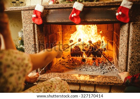 Family roasting marshmallows by the fire. Cozy chalet home with fireplace decorated with traditional Christmas ornaments. Cozy relaxed magical atmosphere in a chalet. Holiday concept.