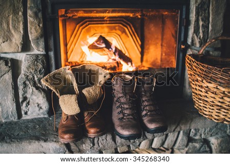 Winter boots in front of a fireplace. Family vintage folk boots drying near the fireside. Warm cozy fireplace in the authentic chalet. Hipster shoes getting warm near the burning fire in a cabin.