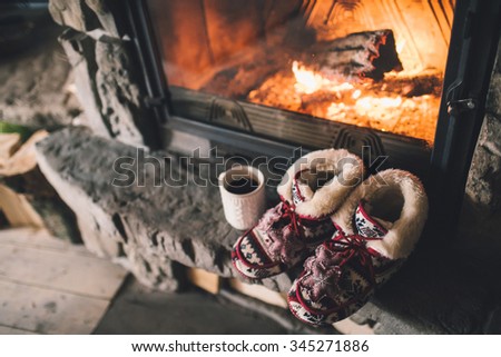 Christmas comfortable slippers by the warm cozy fireplace. Relaxing atmosphere in a chalet by authentic vintage fireside with a cup of hot drink. Winter and Christmas holidays concept.