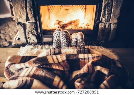 Feet in woollen socks by the Christmas fireplace. Couple sitting under the blanket, relaxes by warm fire and warming up their feet in woollen socks. Winter and Christmas holidays concept.