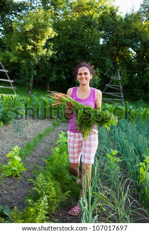 Young gardener woman in her garden, holding vegetables