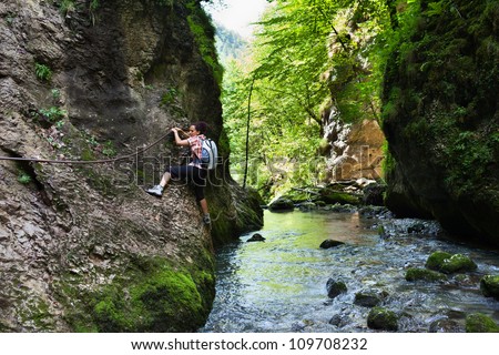 Woman climbing mountain wall over a river in a canyon