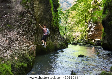 Woman climbing mountain wall over a river in a canyon