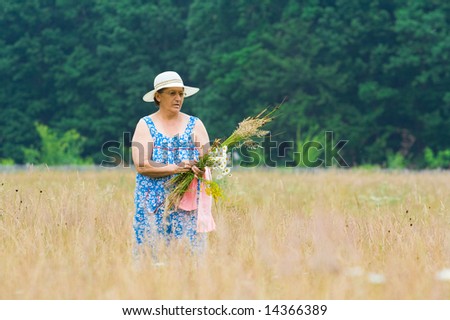 Portrait of an old woman with hat picking flowers near a forest