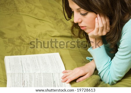 Pretty girl reading a book, sitting on a bed with green sheets