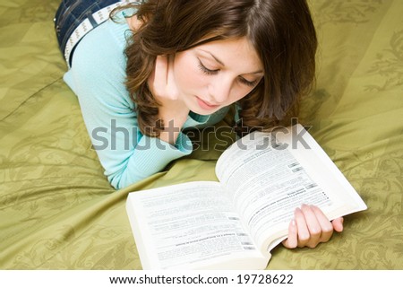 Pretty girl reading a book, sitting on a bed with green sheets