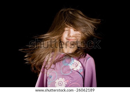 Portrait of a five years old girl flipping her hair, isolated on black