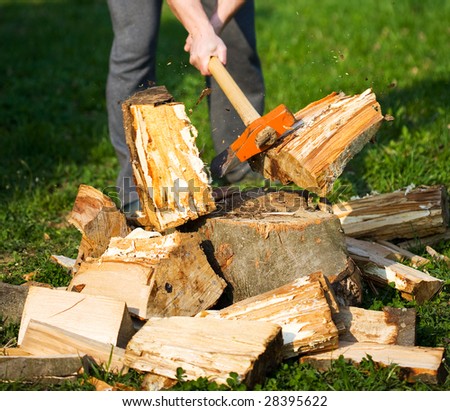 Hands of a strong man splitting wood with an axe, focus is on the axe, motion freezing in the moment it split