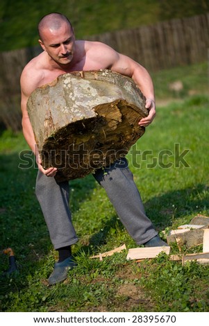 Strong man lifting a huge log, outdoor scene