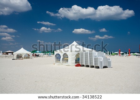 Landscape at seaside with tents and umbrellas on the beach, under blue sky with fluffy clouds