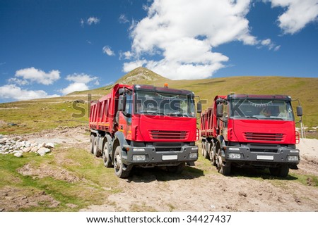 Two large red dump trucks at construction site, in a sunny summer day