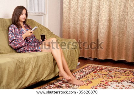Young lady with remote control in her hand sitting on sofa, watching tv