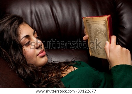 Beautiful young ethnic lady reading a vintage book on a leather sofa