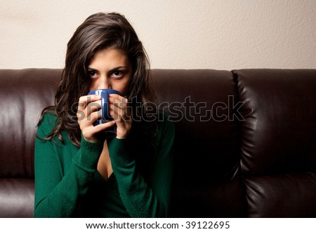 Beautiful brunette drinking tea or coffee while sitting on a leather couch