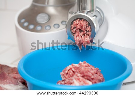 Meat grinder in kitchen and a blue bowl with mincemeat