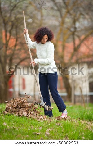 Young redhead pretty country girl using a rake to clean up of the fallen leaves