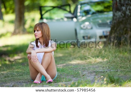 Young woman sitting on the ground near by her car, in the forest