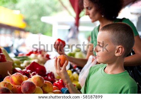 Cute boy with his mother buying fresh vegetables at the farmer\'s market