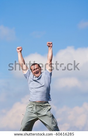 Happy young man stretching his arms outdoor against blue sky, lots of copyspace
