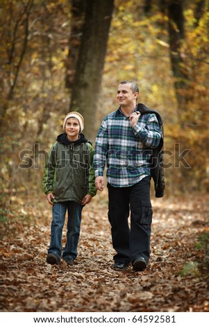 Father and son talking a walk outdoor in a forest, in an autumn day