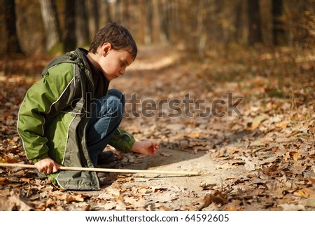 Cute kid writing on the ground with a stick in the forest