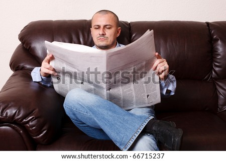 Young man reading newspaper on a leather sofa