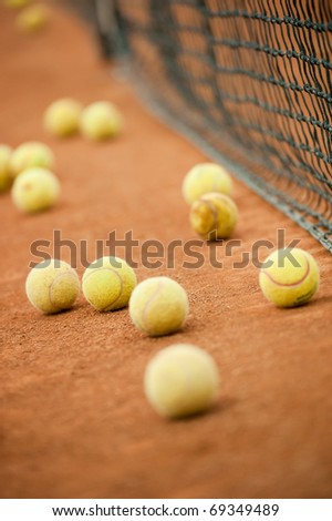 Many yellow tennis balls on a slag field near the net