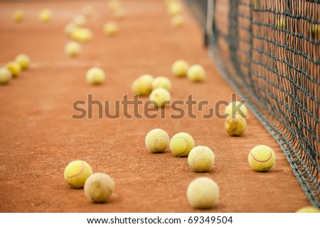 Many yellow tennis balls on a slag field near the net