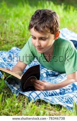 Portrait of a boy reading a book outdoor on the grass