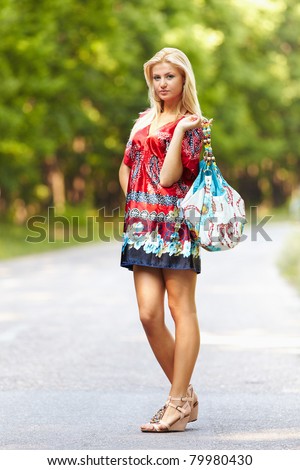 Full length portrait of a young blond woman in colorful dress with purse outdoor