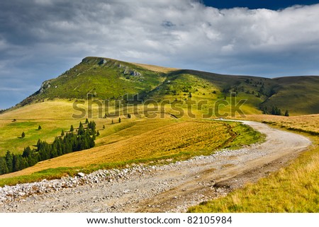 Landscape with dirt road in the mountains under cloudy sky