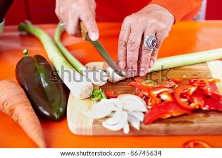 Senior woman hands chopping vegetables on a wooden board in the kitchen