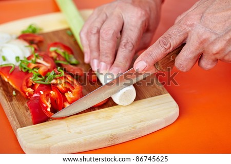 Senior woman hands chopping vegetables on a wooden board in the kitchen