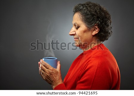 Closeup profile of an elderly senior woman with hot coffee or tea in a cup, on gray background