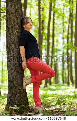 Full lenght portrait of a young beautiful woman leaning on a tree in the woods