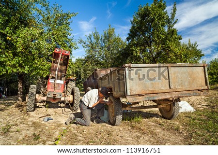 Senior farmer repairing his tractor outdoor in the field
