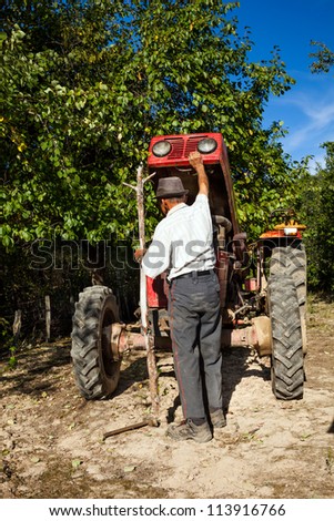 Senior farmer repairing his tractor outdoor in the field