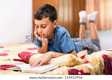 Studio portrait of a schoolboy reading a textbook while lying in bed