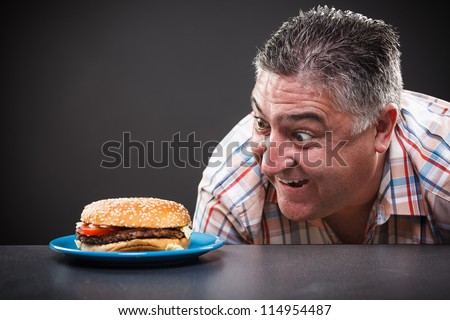 Portrait of a greedy man looking at burger on gray background
