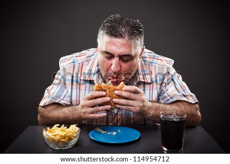 Portrait of a greedy fat man eating burger on gray background